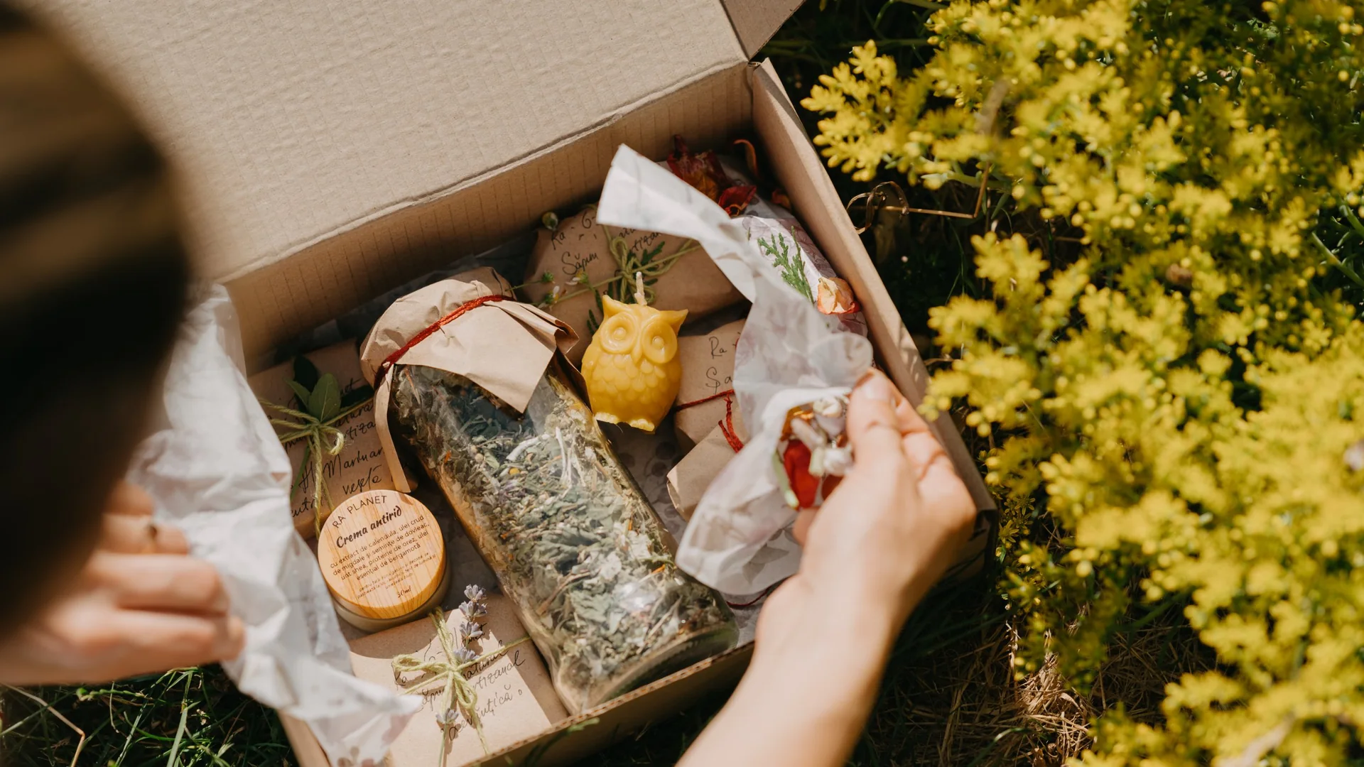 Open gift box with herbs, honey and soap among yellow flowers