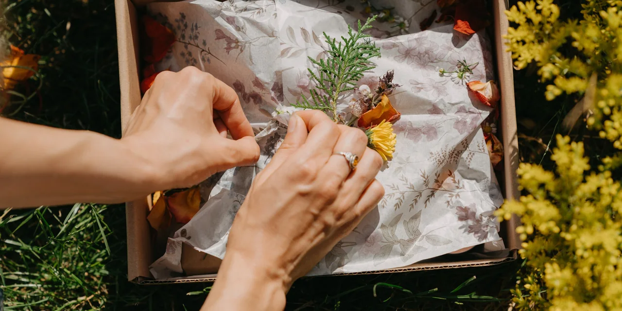 Hands wrapping a gift box with dried flowers